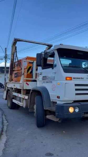 Caminhão poliguindaste transportando caçamba